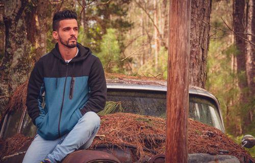 Free A man in casual attire sitting on an overgrown vintage car in a forest. Stock Photo