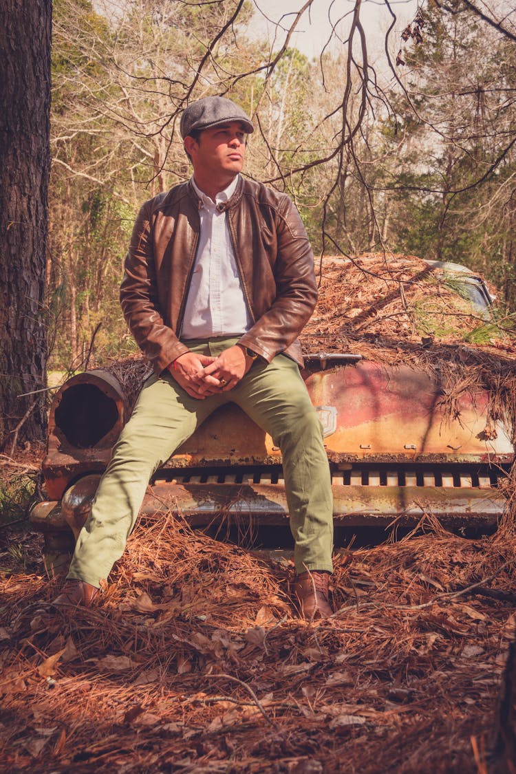 Man Sitting On Old Car Hood In Forest