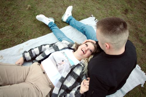 Free Joyful couple enjoying a playful moment on a blanket in a park setting. Stock Photo