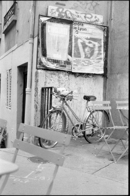 A classic bicycle leans against a wall with posters in a city setting, black and white.