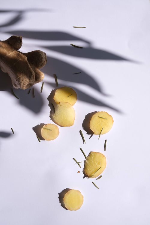 Free Ginger slices with rosemary on a white surface, creatively lit with shadows. Perfect for food and culinary themes. Stock Photo