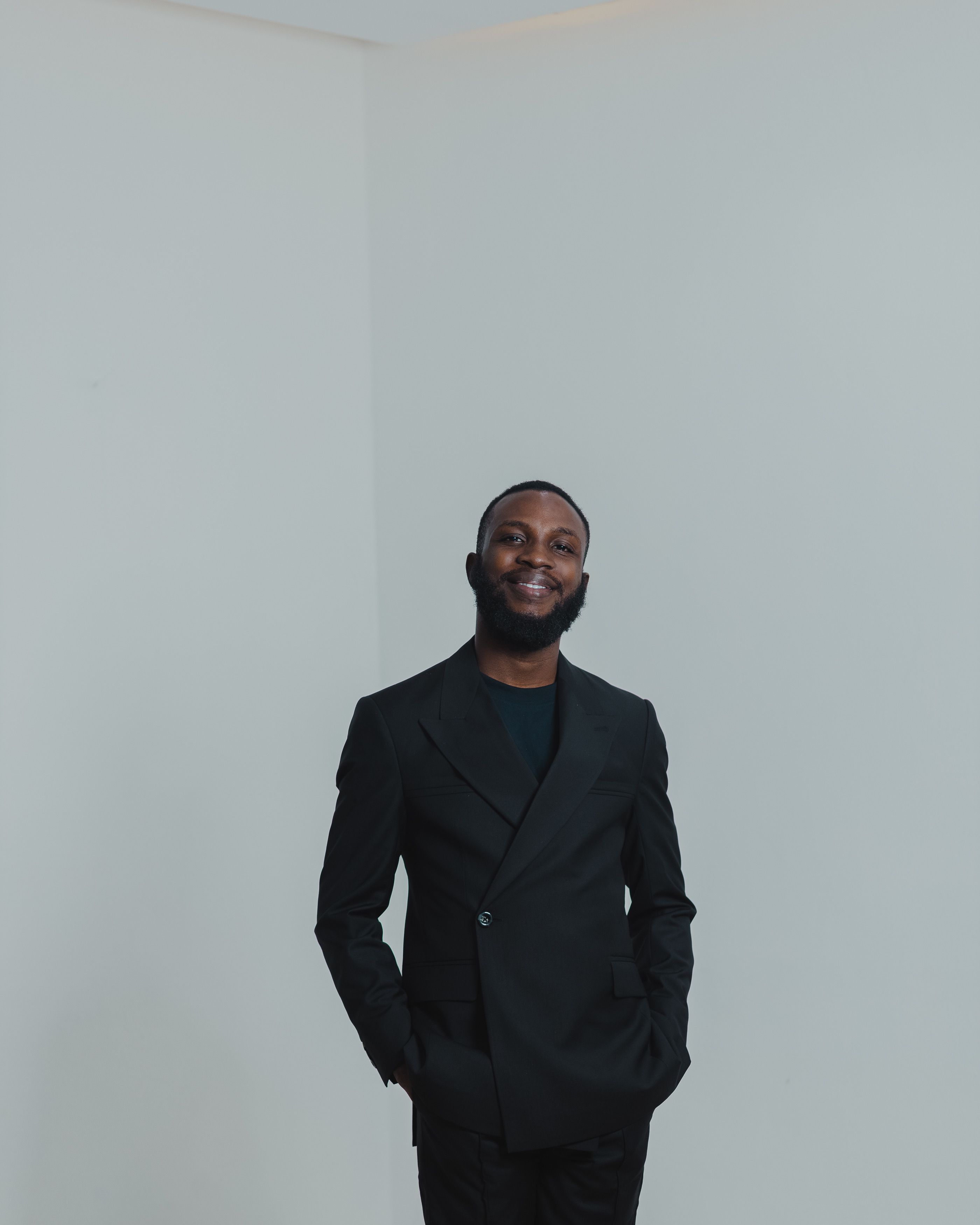 Portrait of a confident young man in a black suit posing in a studio with a white background.