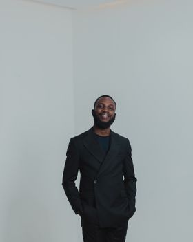 Portrait of a confident young man in a black suit posing in a studio with a white background.