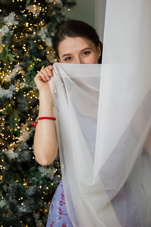 Woman Posing behind Curtain and with Christmas Tree behind