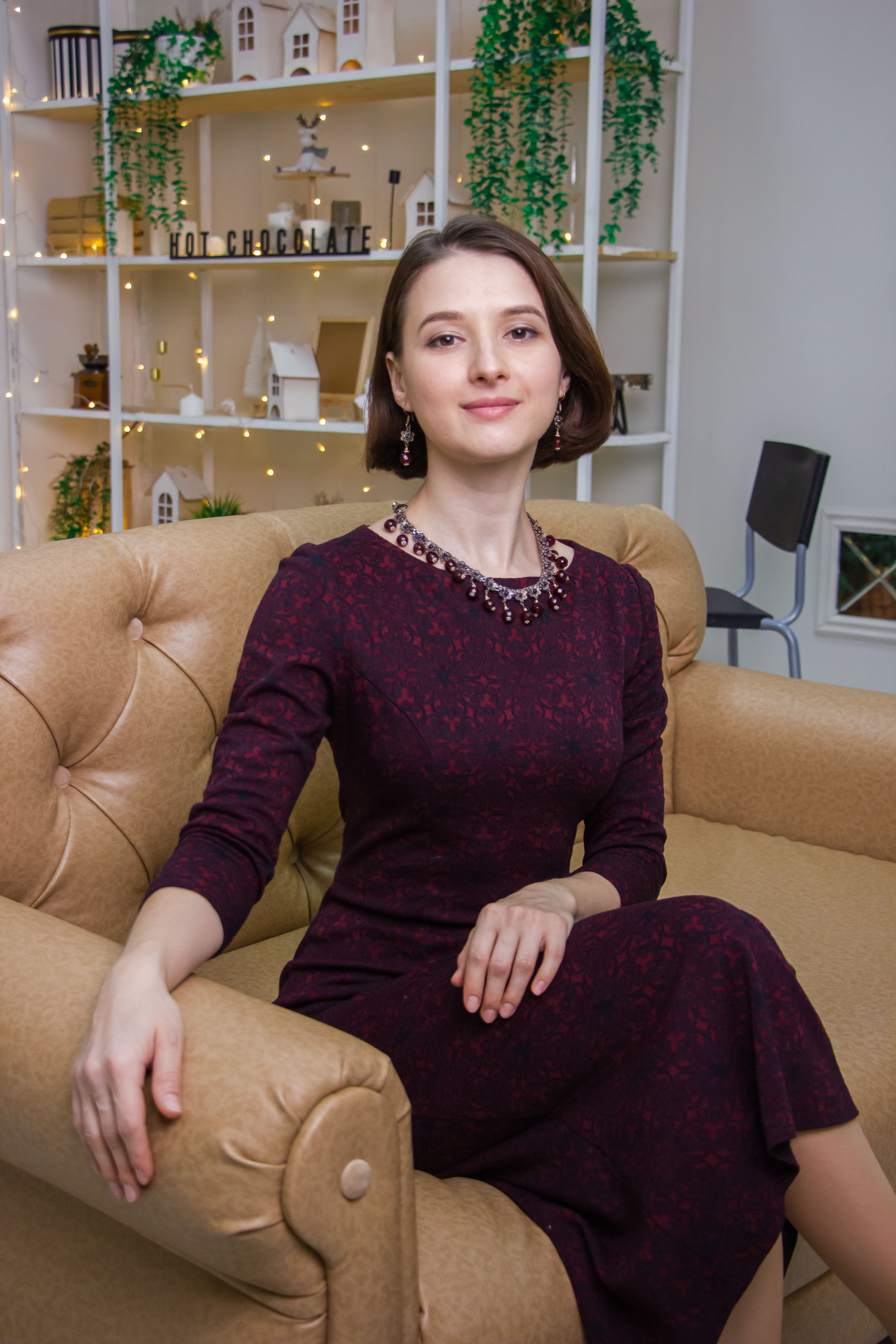 Fashionable woman in a stylish dress sitting indoors, exuding elegance.