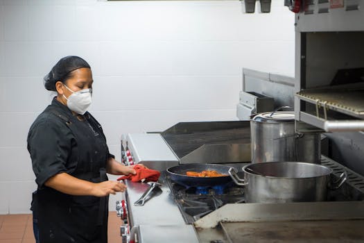 Chef busy at work in a commercial kitchen, preparing dishes while wearing a protective mask.