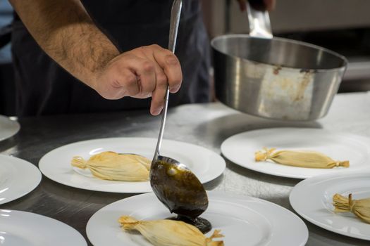 Chef plating gourmet dishes with sauce in a professional kitchen setting, showcasing culinary skills.