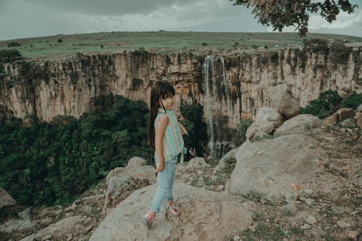 A child enjoying the scenic view of a waterfall from a rocky cliff, perfect for travel and adventure themes.