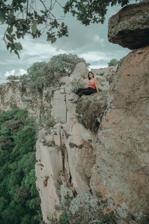 Free A woman sitting on a cliff edge surrounded by nature, showcasing a scenic canyon view. Stock Photo