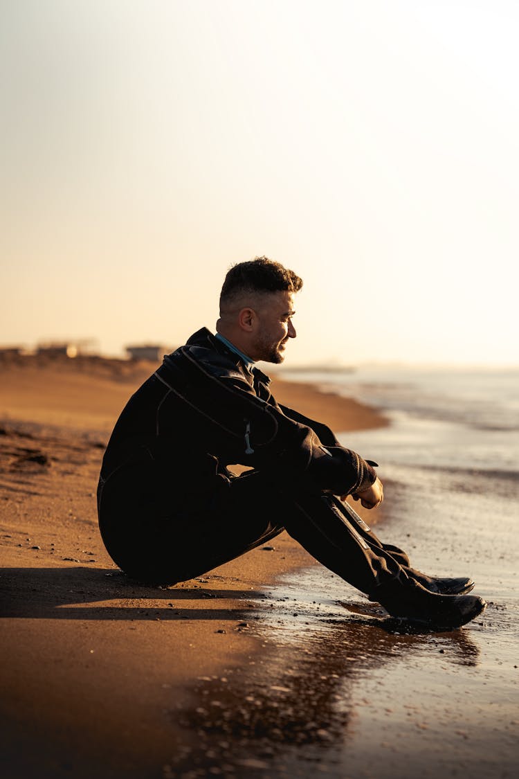 Man Sitting Alone On A Sandy Beach At Sunset