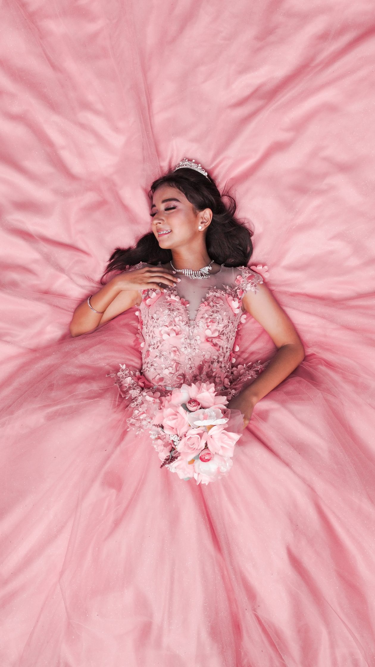Young woman in a pink gown and tiara lying on pink satin fabric