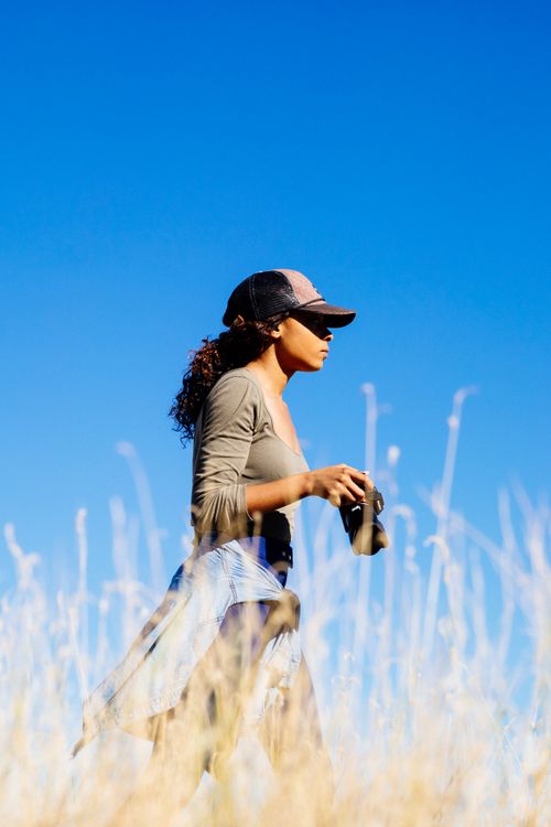 Free A woman with binoculars walks through a sunny field, exploring nature. Stock Photo