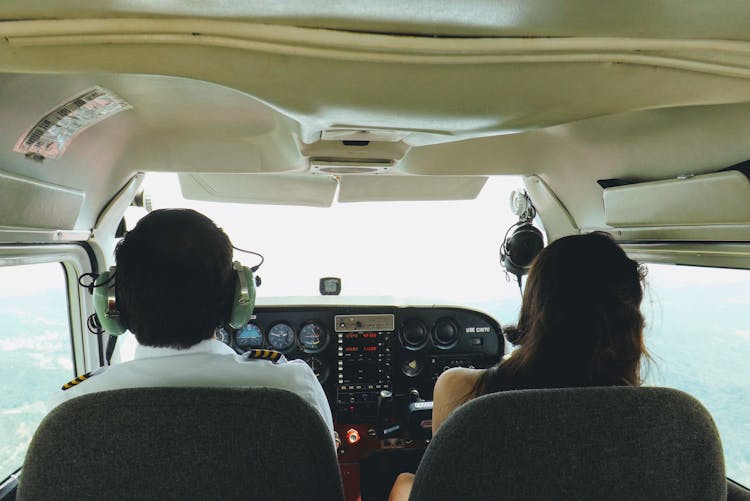 Back View Of A Pilot And A Woman Sitting Next To Him In A Plane 