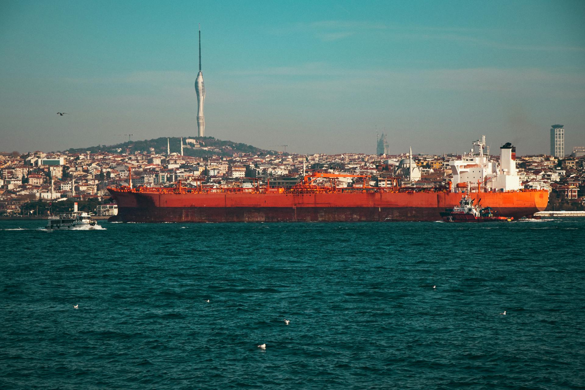 A large oil tanker navigates the Bosphorus Strait with Istanbul's skyline and Camlica Tower in the background.