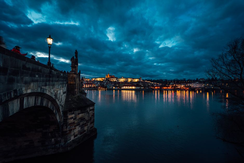 Illuminated Charles Bridge at dusk with Prague skyline reflection