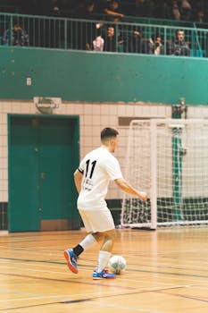 A male soccer player dribbling indoors, wearing sportswear during a game.