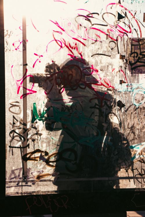 Free Silhouette of a photographer taking pictures in front of a graffiti-covered wall, creating an artistic urban scene. Stock Photo