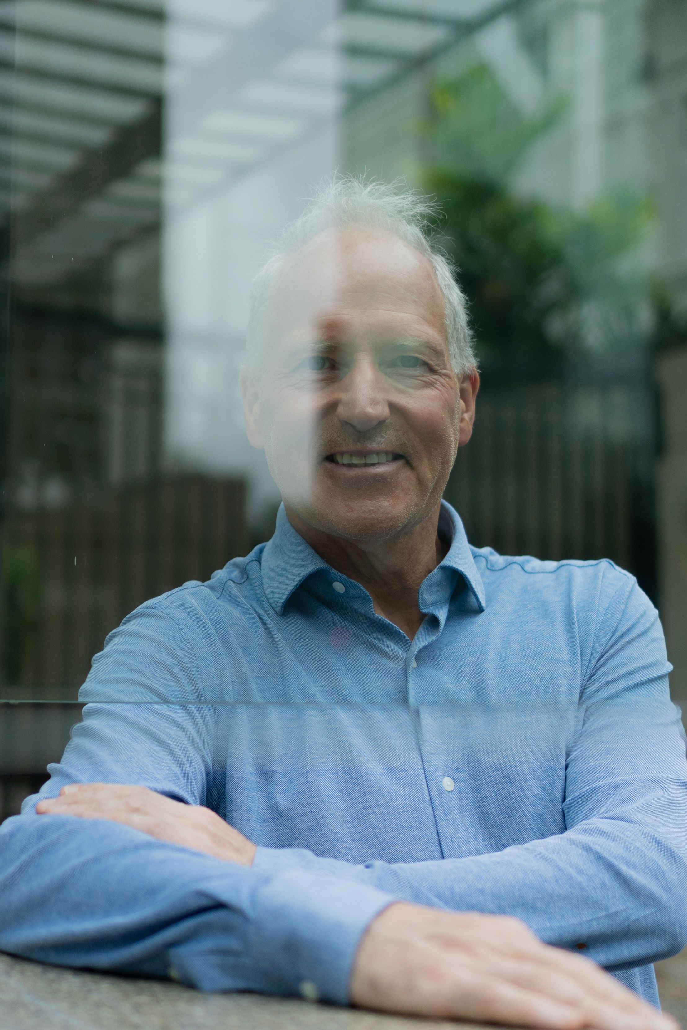 Elderly man with gray hair smiling through a glass window.