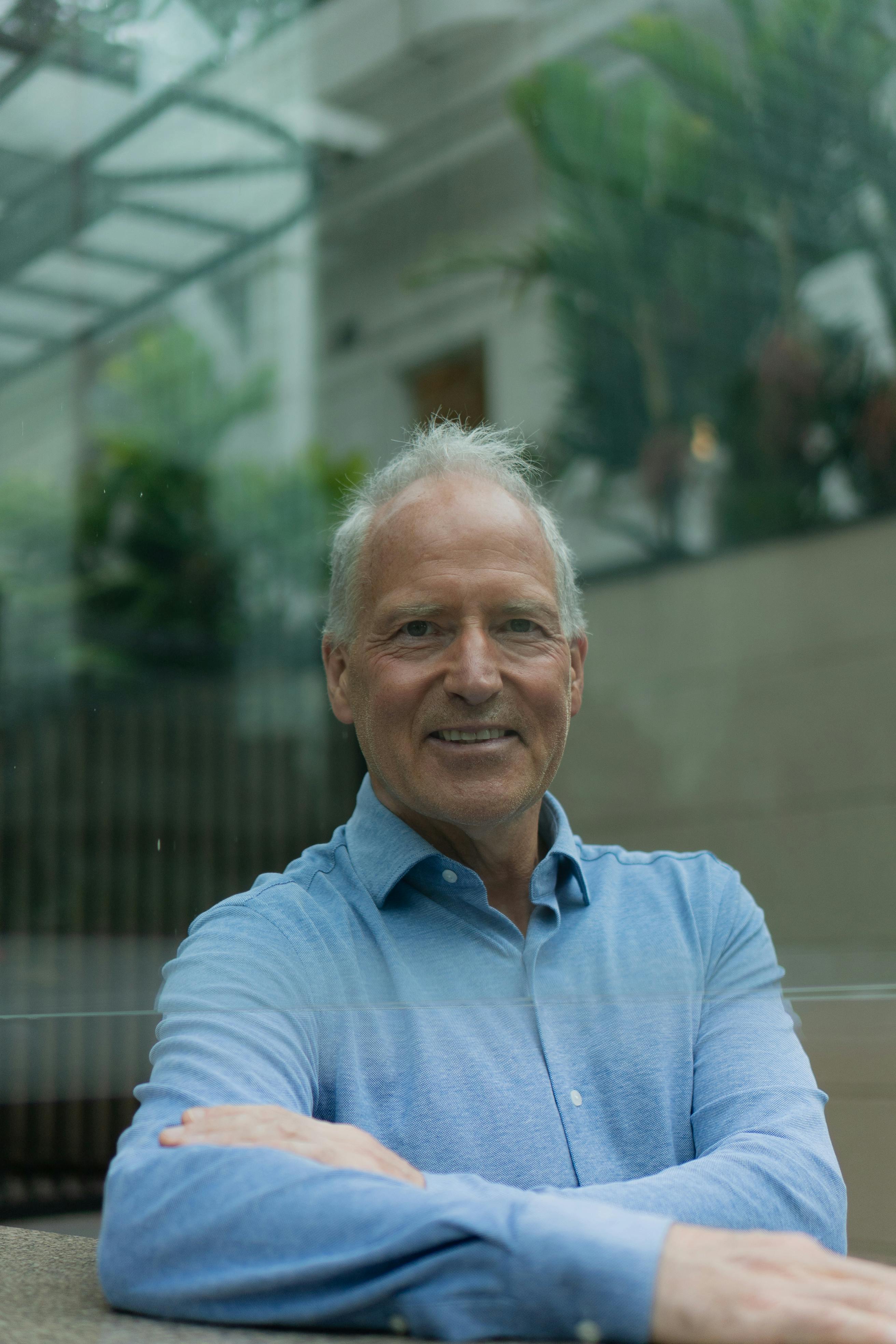 Elderly man smiling inside a modern glass architecture with greenery.