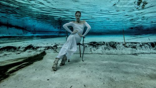 Free A young woman posing gracefully underwater, wearing a stylish white dress and high heels. Stock Photo