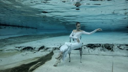 Free A captivating underwater fashion shoot featuring a caucasian woman in a white dress, posing elegantly. Stock Photo