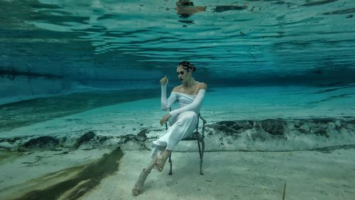 Free A fashion model poses underwater in a white dress, sitting on a chair. Stock Photo