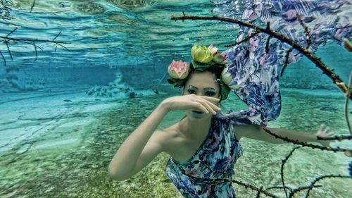 Free An artistic underwater photo of a woman with floral accessories and flowing dress, surrounded by branches. Stock Photo