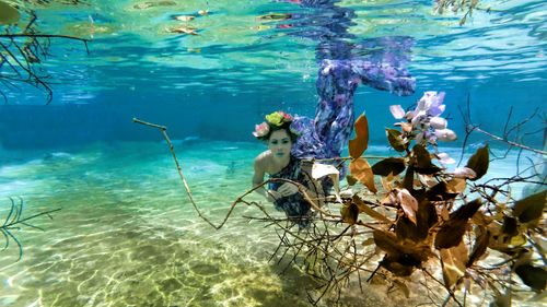 Free Enchanting underwater fashion shot of a woman in floral attire and crown, surrounded by leaves. Stock Photo