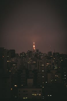 夜晚，一座发光的塔楼在城市建筑中若隐若现，为天际线增添了戏剧性