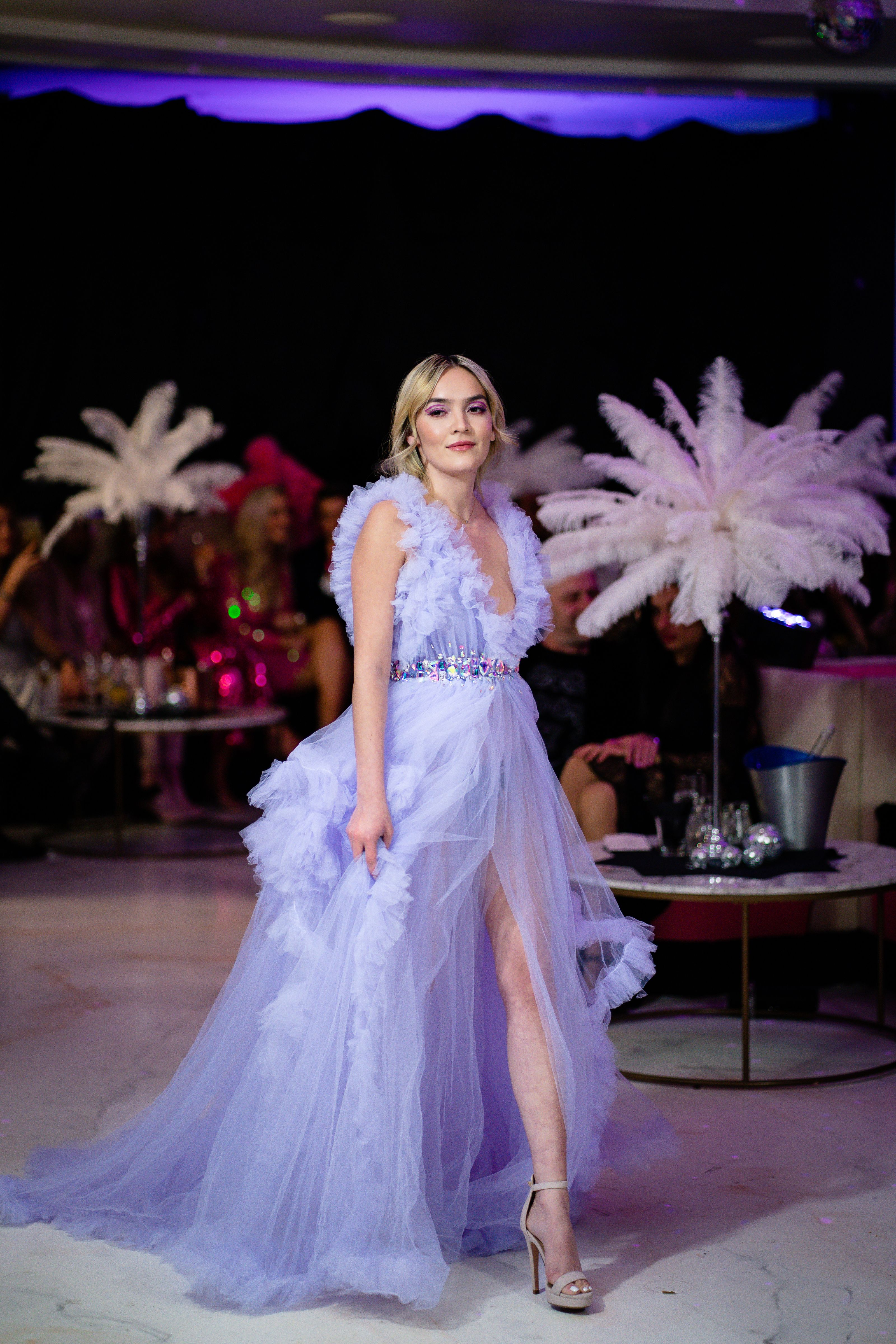 Modelo de moda exibindo um elegante vestido azul em um evento interno glamouroso.