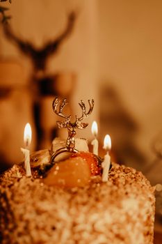 Close-up shot of a caramel cake with decorative candles and a reindeer topper, creating a warm and festive ambiance.