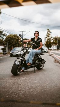 Smiling young woman sitting on a moped in a bustling urban street setting.