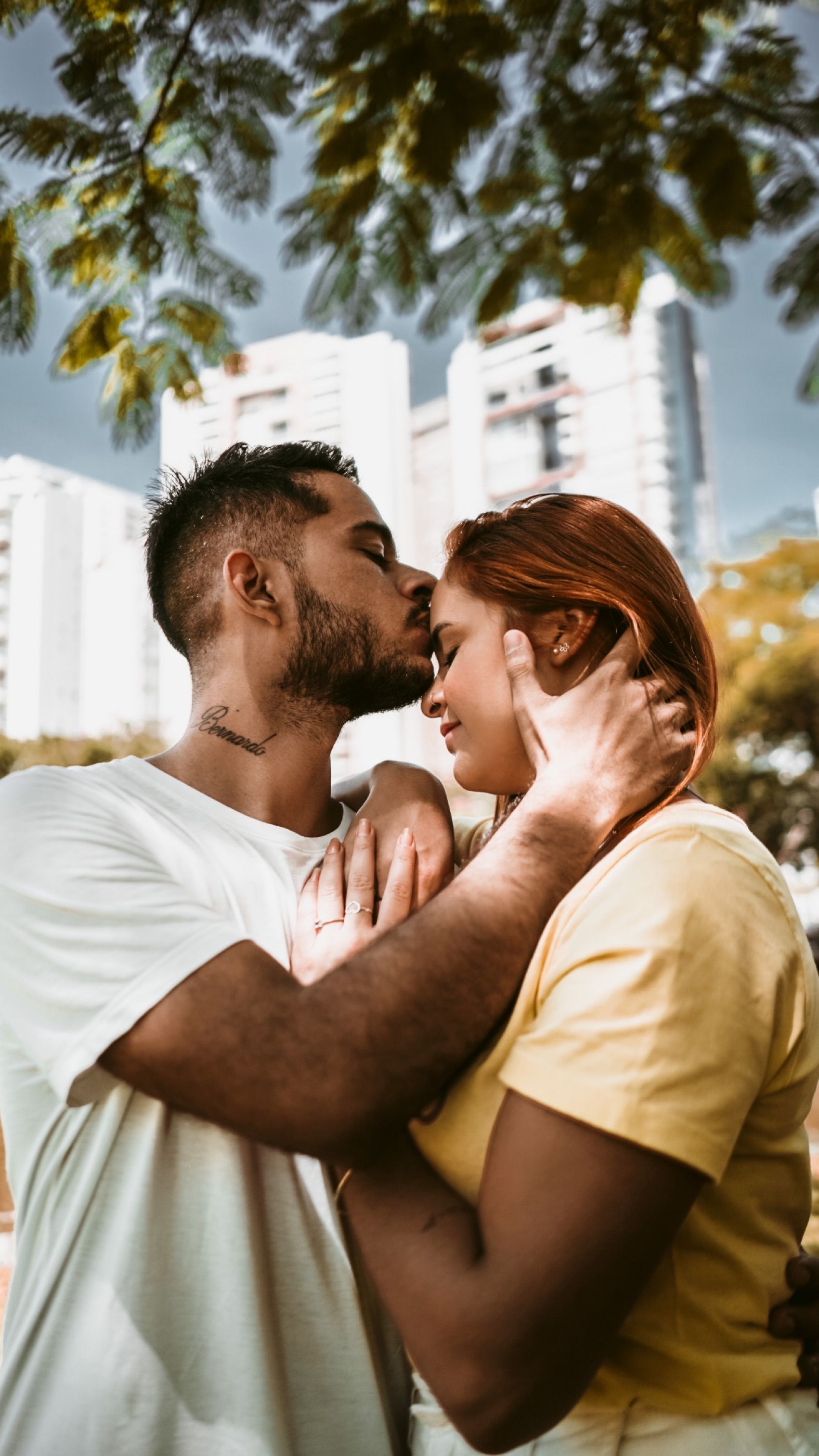 A loving couple shares a tender kiss under city trees, embodying youthful romance.
