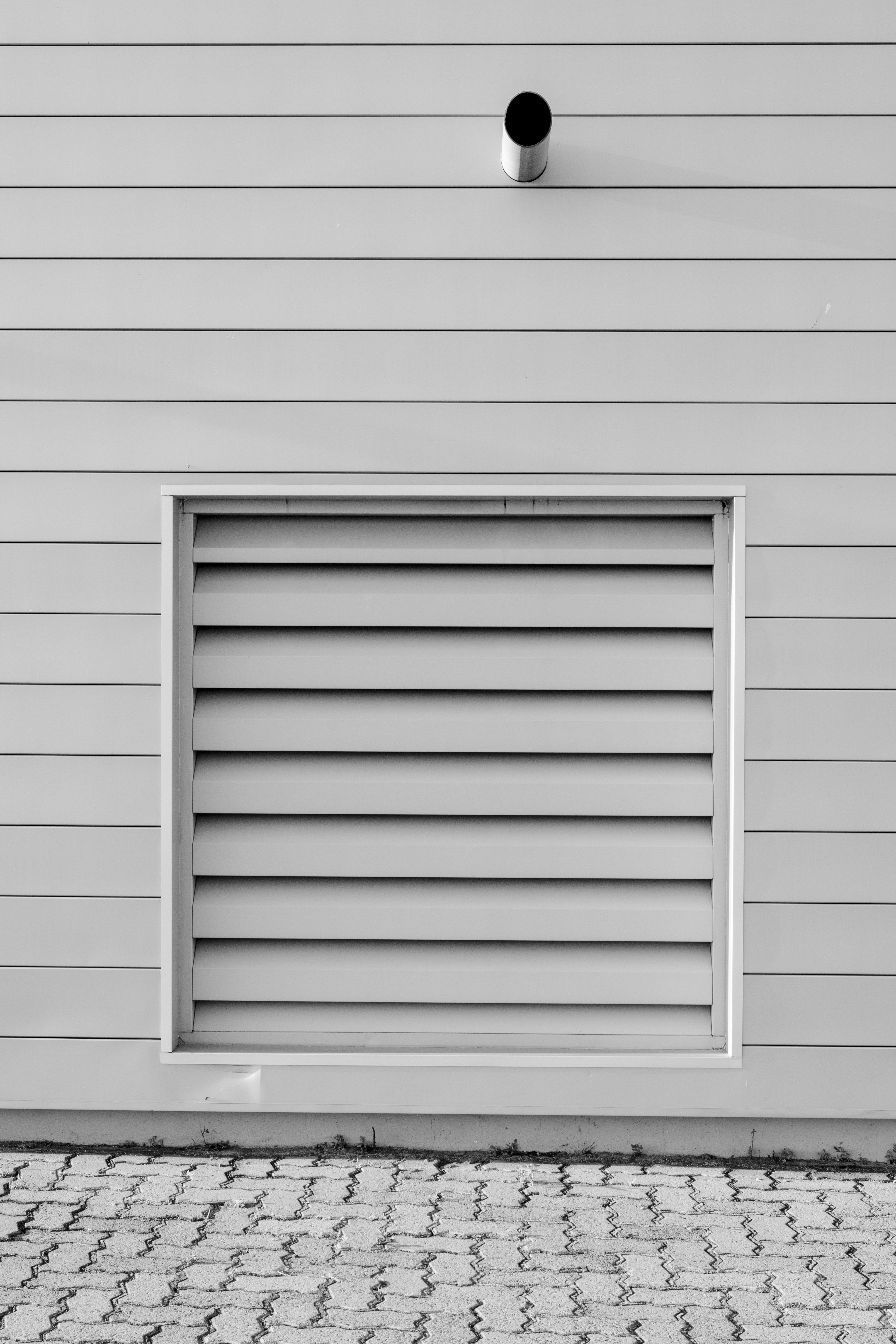 Black and white minimalist photo of an exterior wall with a vent and piping, capturing modern architecture.