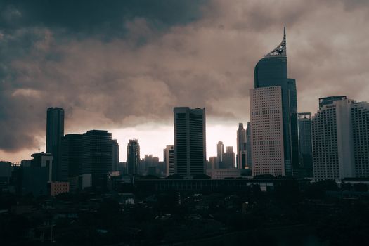 A dramatic view of the Jakarta skyline under heavy, dark clouds, creating an urban silhouette.