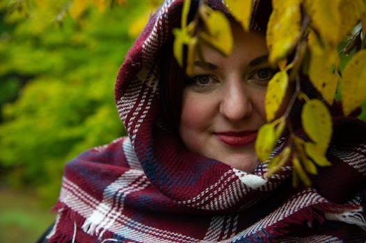 A captivating portrait of a woman wrapped in a scarf amidst fall foliage.