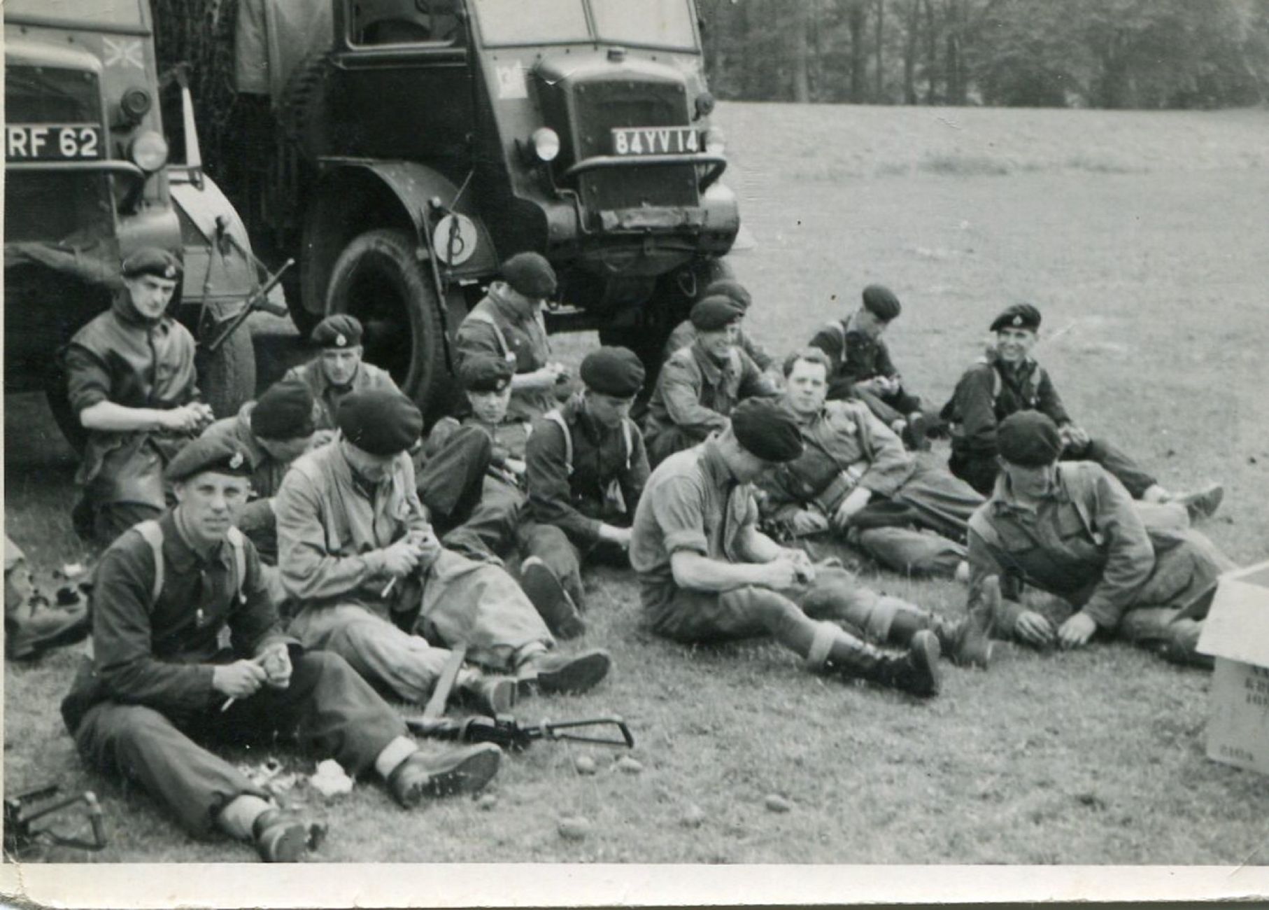 British soldiers resting in a field beside military trucks, in black and white.