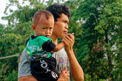 Man Carrying Baby Near Green Trees