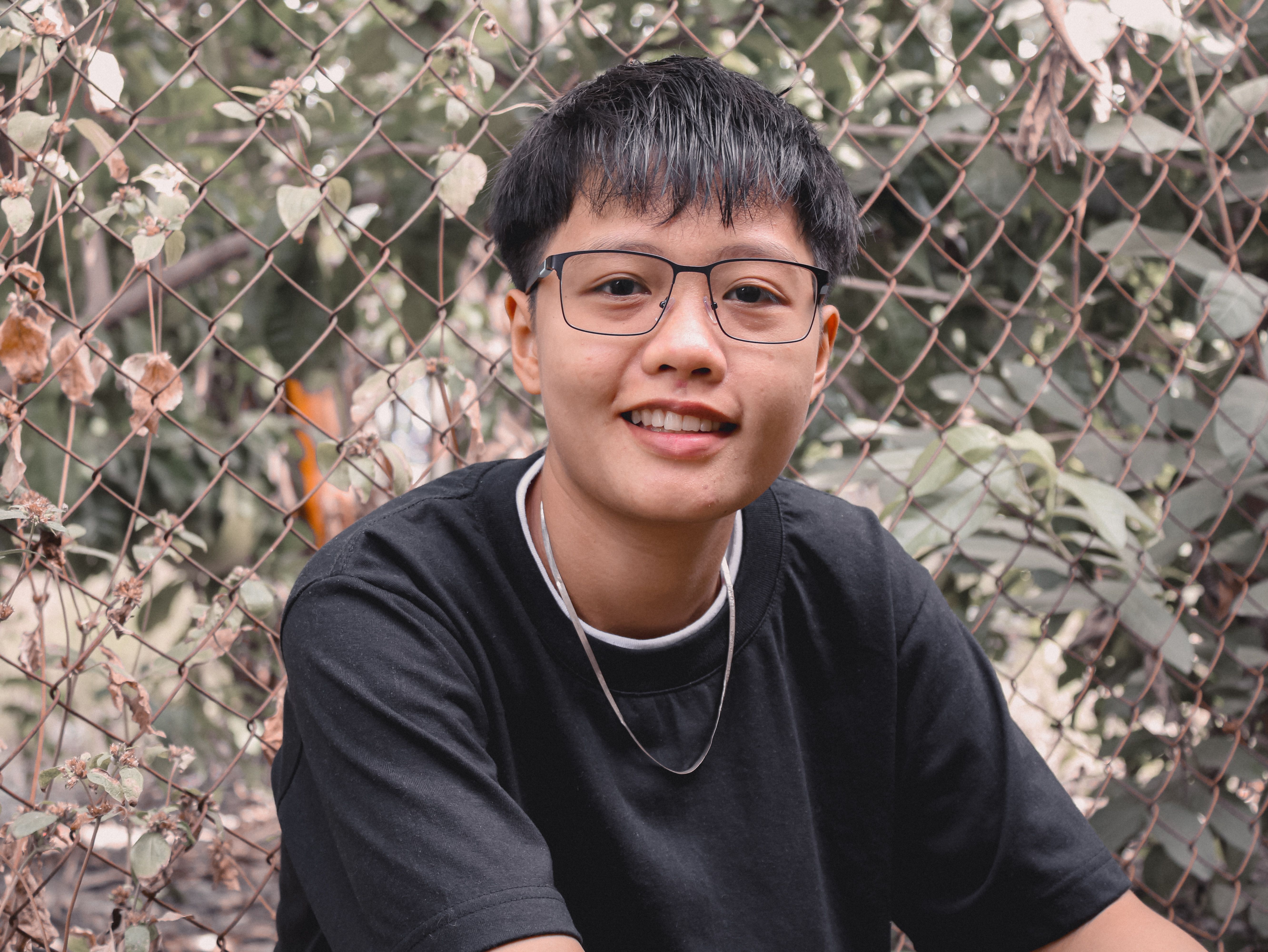 A young individual with glasses smiles outdoors, showing confidence and style.