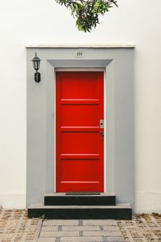 Bright red wooden door with surrounding grey frame and lantern in an urban environment.