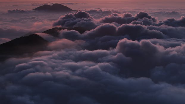 Stunning aerial view of mountain peaks emerging through a sea of clouds at sunrise.