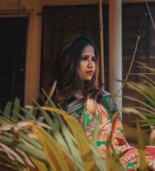 Brunette woman in a colorful saree sitting thoughtfully in an outdoor setting.