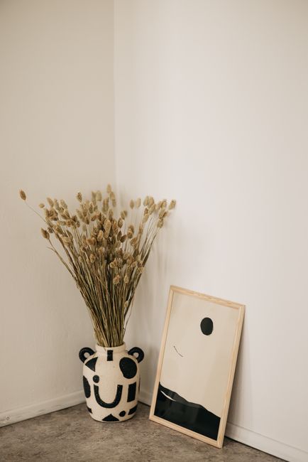 Elegant minimalist corner featuring a decorative pottery vase with dried flowers and abstract artwork.