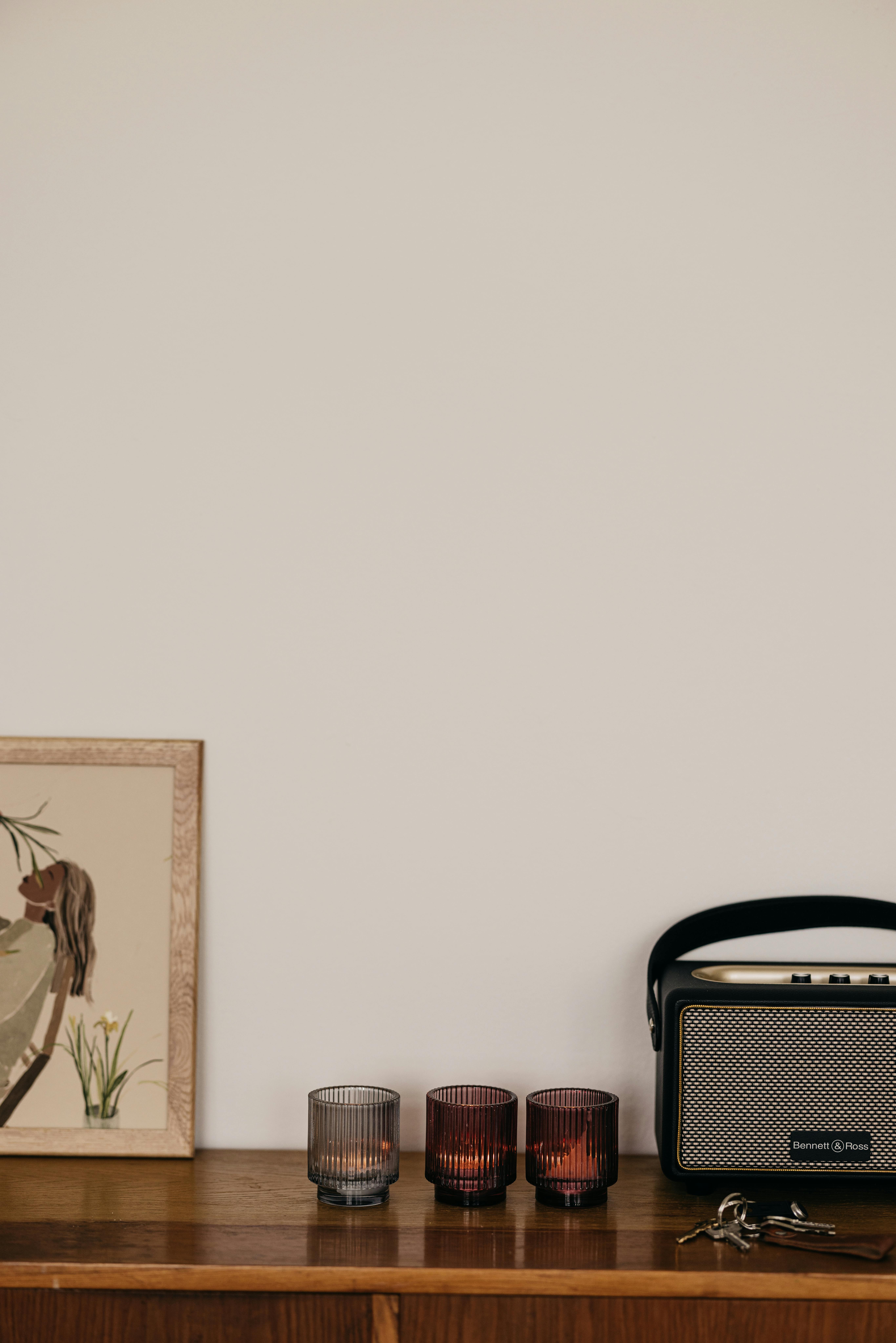 A minimalist shelf featuring candles, artwork, and a retro radio against a white wall.