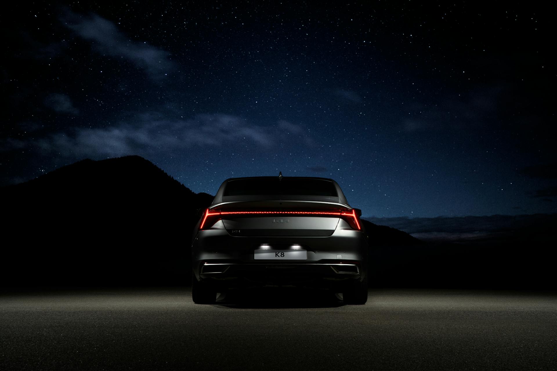 Sleek black car with illuminated tail lights parked beneath a starry sky, exuding modern elegance.