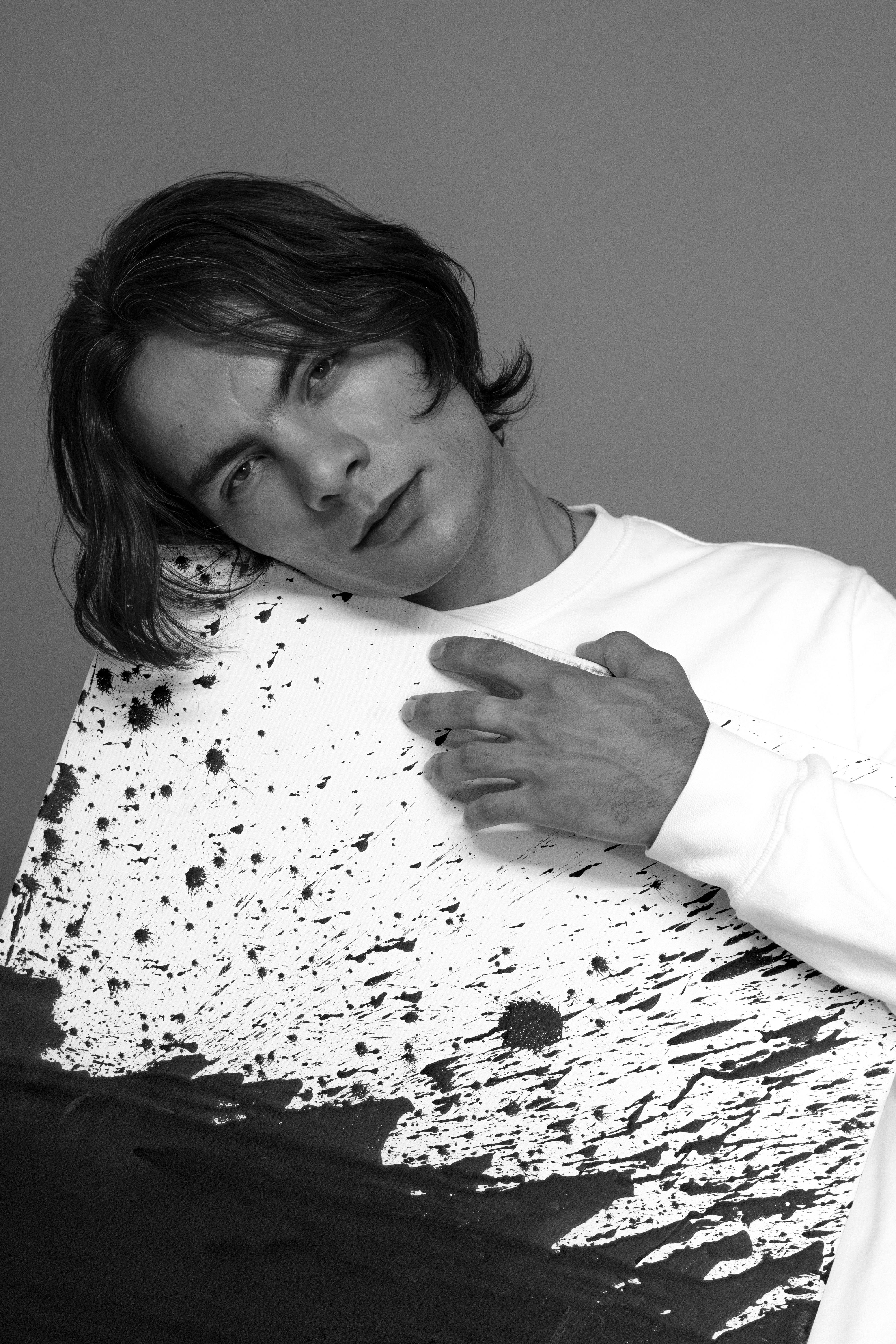 A contemplative man holding an abstract painting in a black and white portrait.