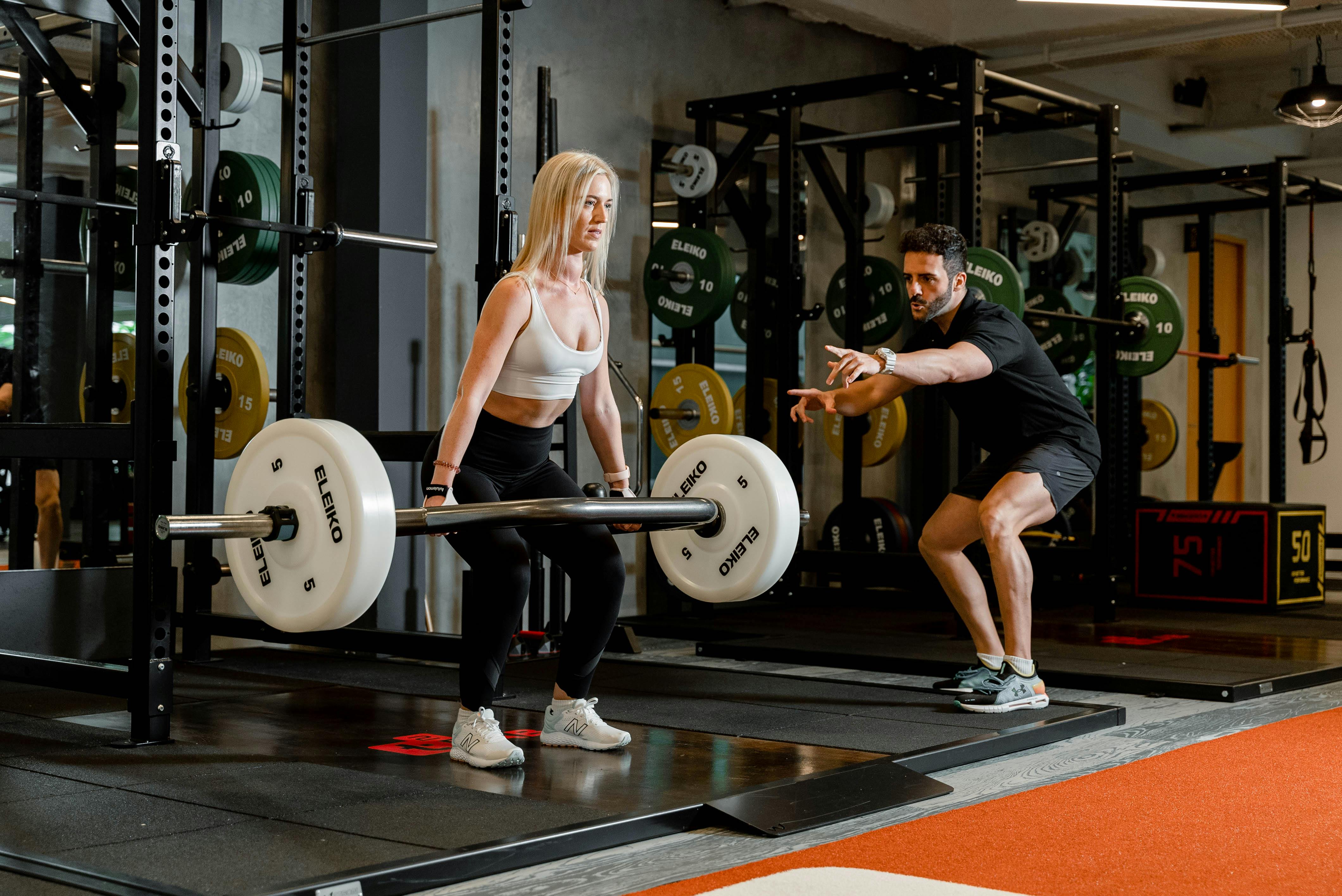 Woman lifting weights under trainer's guidance in Singapore gym, focusing on strength training.