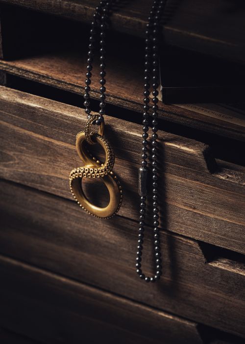 Free Brass infinity pendant on black beaded necklace elegantly draped over a wooden drawer. Stock Photo