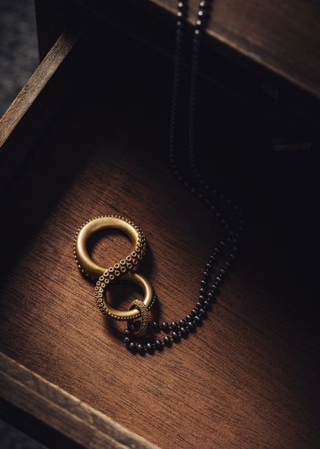 Stunning brass infinity pendant necklace displayed in an open wooden drawer.