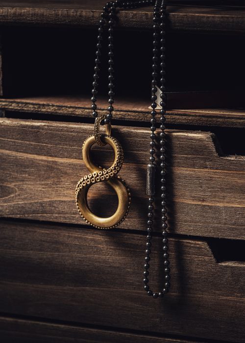 Free A striking octopus-inspired necklace with infinity symbol design, draped over rustic wooden drawers. Stock Photo
